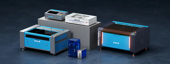Studio lineup of OMTech CO2 cabinet laser machines, including a Pronto 60, with additional desktop units and accessories on display.